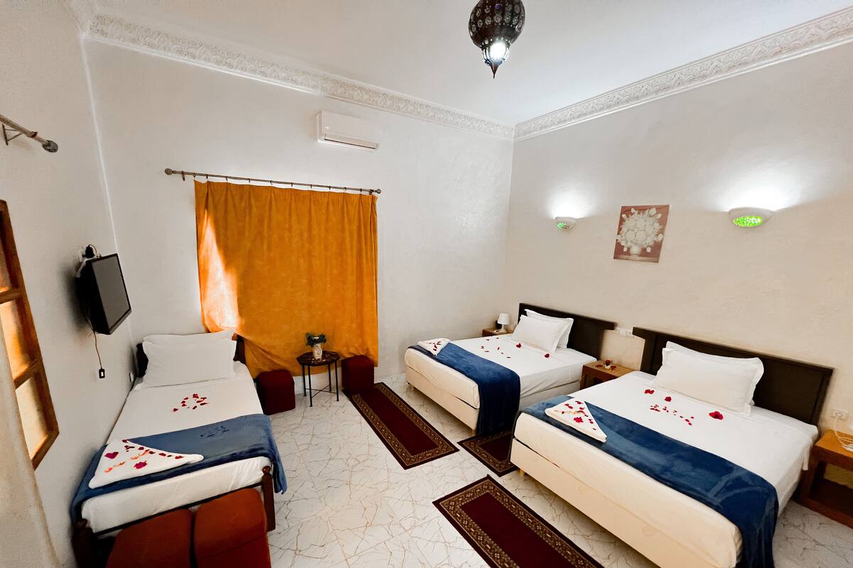Une chambre d’hôtel avec deux lits, une télévision, une petite table et une fenêtre avec des rideaux.