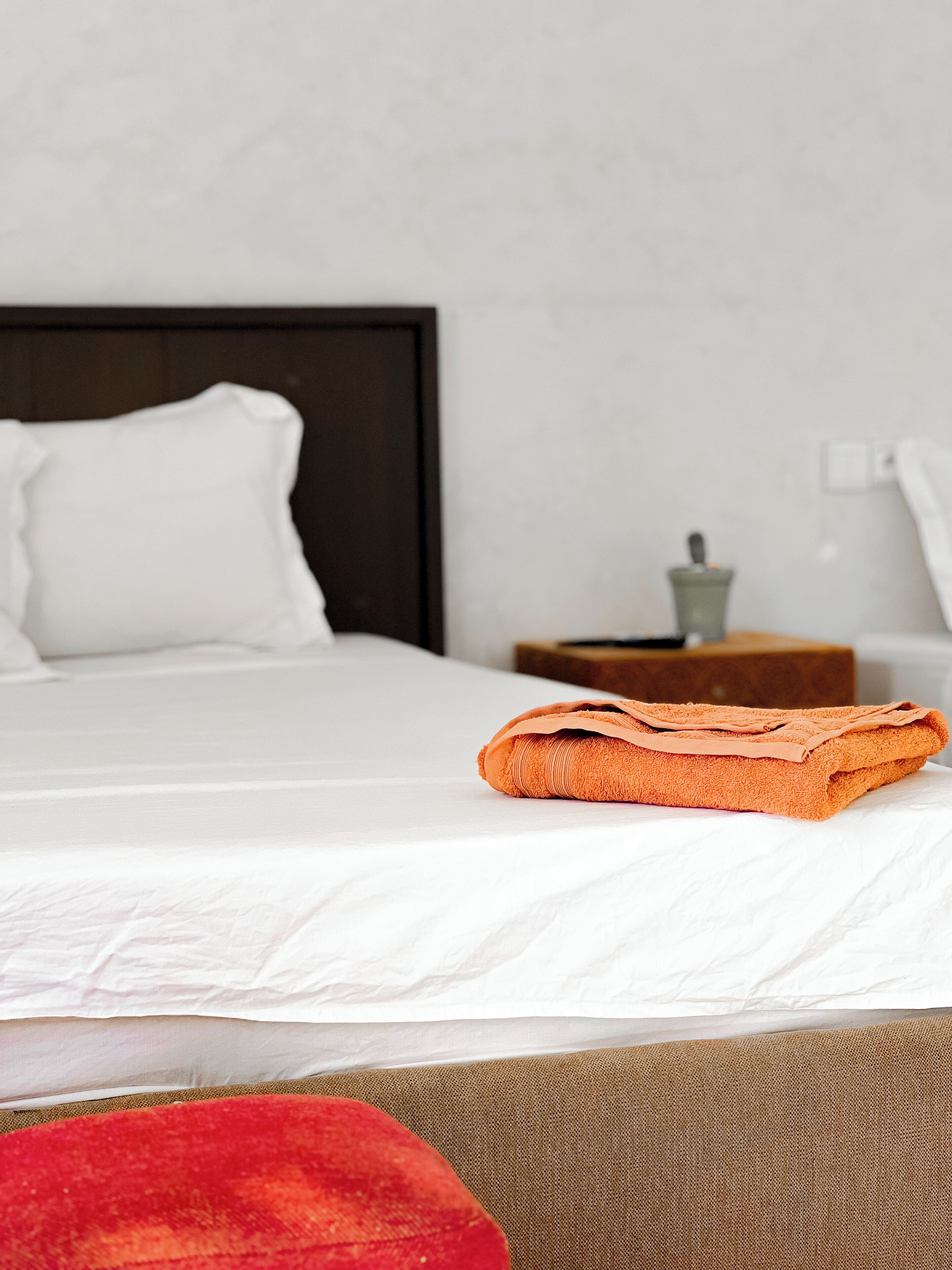 A neatly made bed with white bedding and an orange towel on the side.