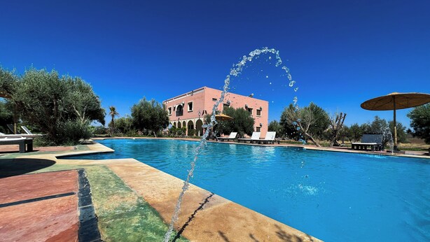 Una piscina amb una font d'aigua, gandules i un edifici al fons.