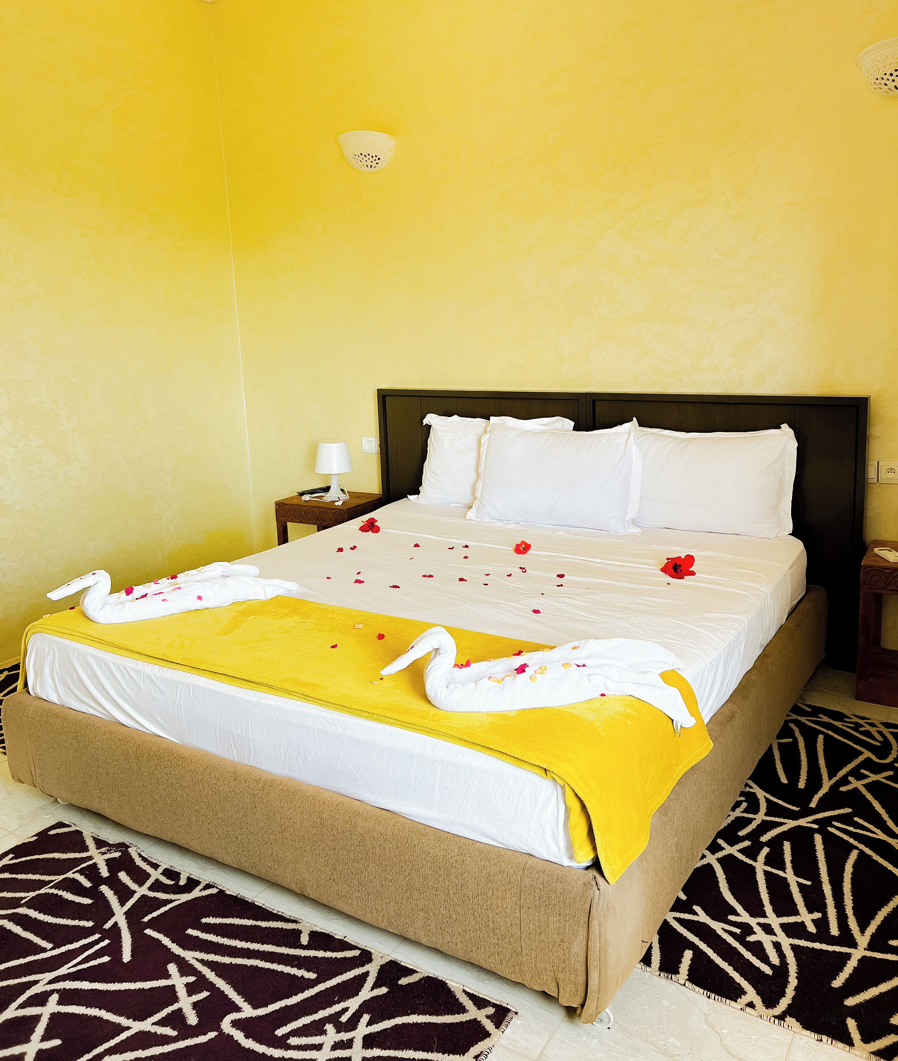 A neatly made bed with a yellow bedspread, white pillows, and a decorative swan towel.
