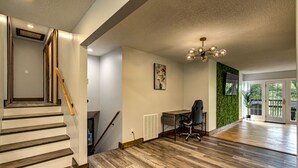 A spacious room with a wooden staircase, a desk with a chair, a green wall, and a ceiling light fixture. - Modern! 4BR, Game Room, Pets, Hot Tub, PS5, 6 min to Dollywood + More! Sleeps 8! (Pigeon Forge)