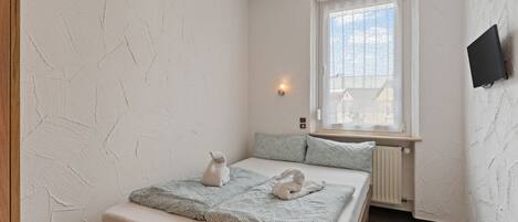 A bedroom with a bed, two pillows, a window, a wall-mounted TV, and a radiator.