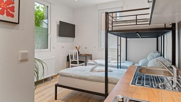 Habitación moderna y luminosa con una cama nido, un escritorio, una silla y un ventanal amplio.