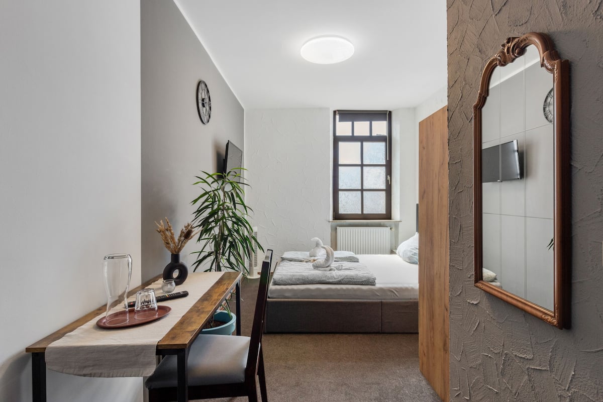 A compact bedroom with a bed, bedside table, and a large mirror.