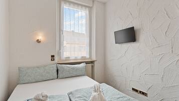 A bedroom with a bed, pillows, a window, a wall-mounted TV, and a wall with a textured pattern.