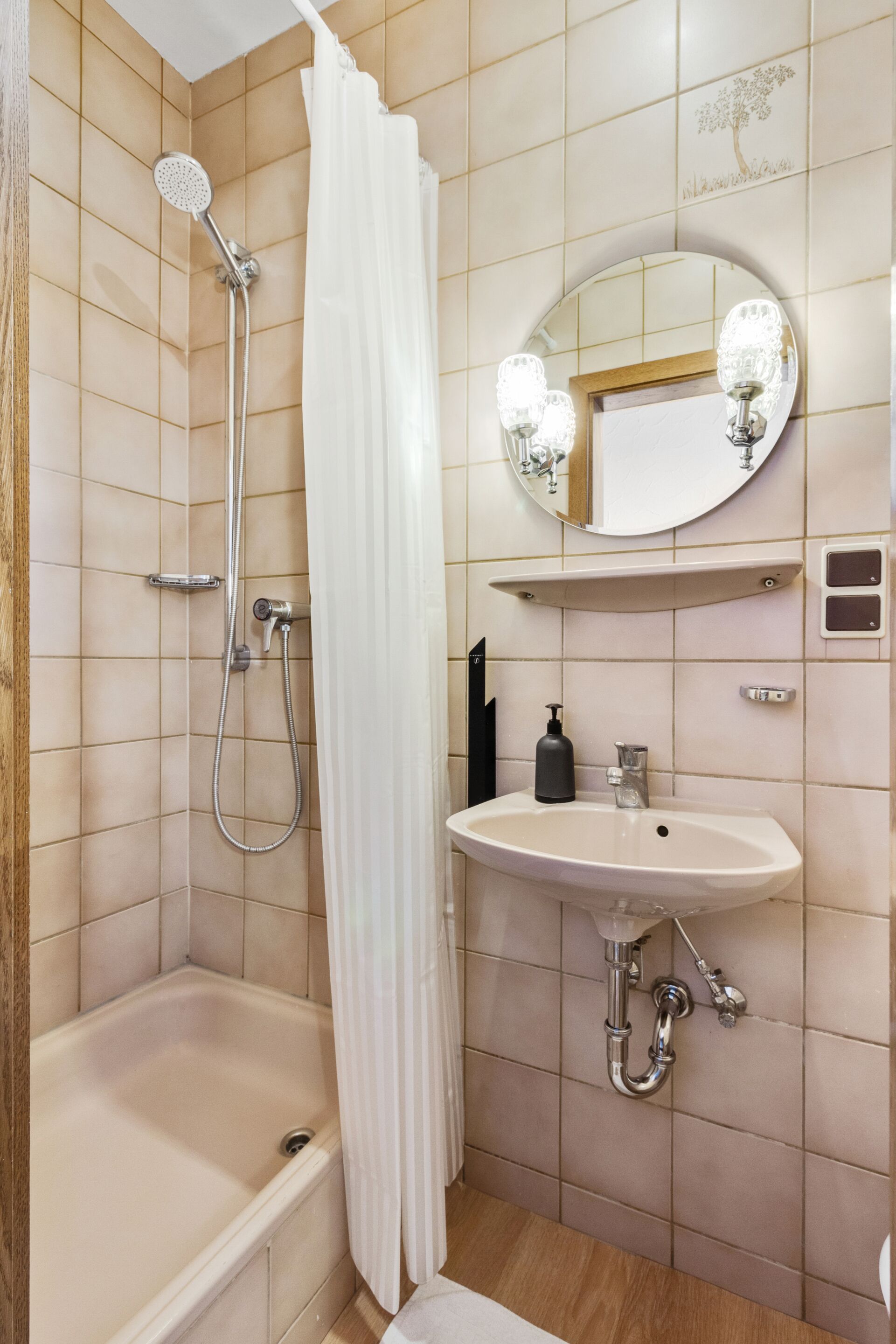 A bathroom with a bathtub, a shower with a curtain, a sink with a mirror above it, and a soap dispenser.