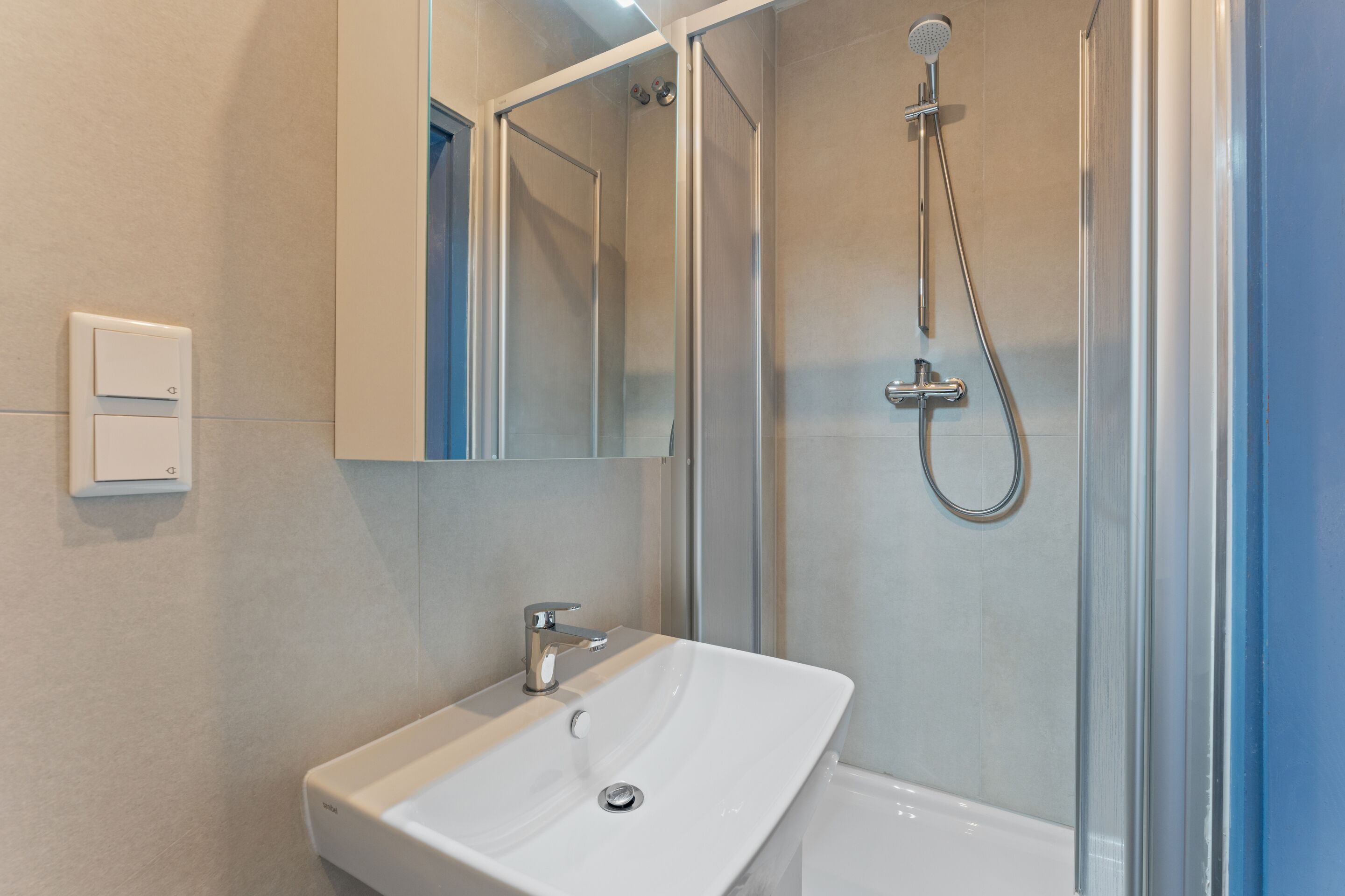 Een moderne badkamer met een douchecabine van glas, een witte wastafel en een spiegel erboven.