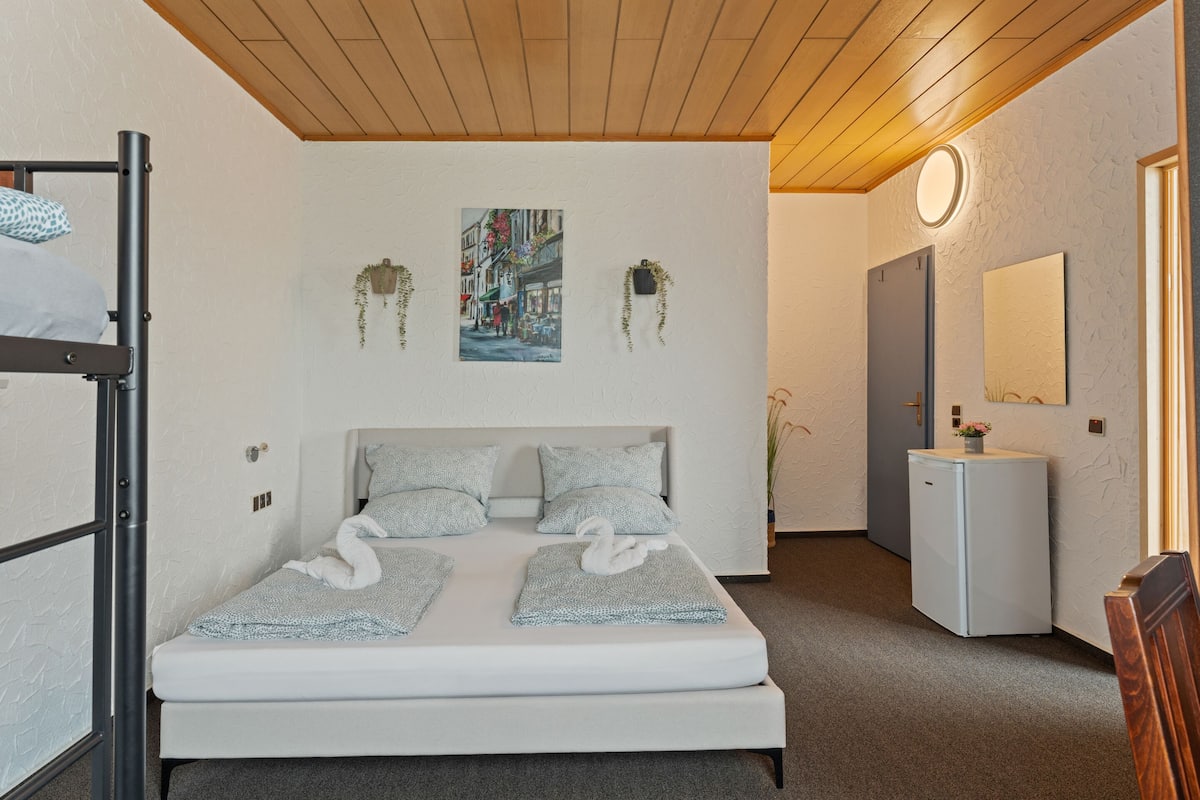 A modern bedroom with a bunk bed, a small bedside table, a mirror, and a wall-mounted picture.