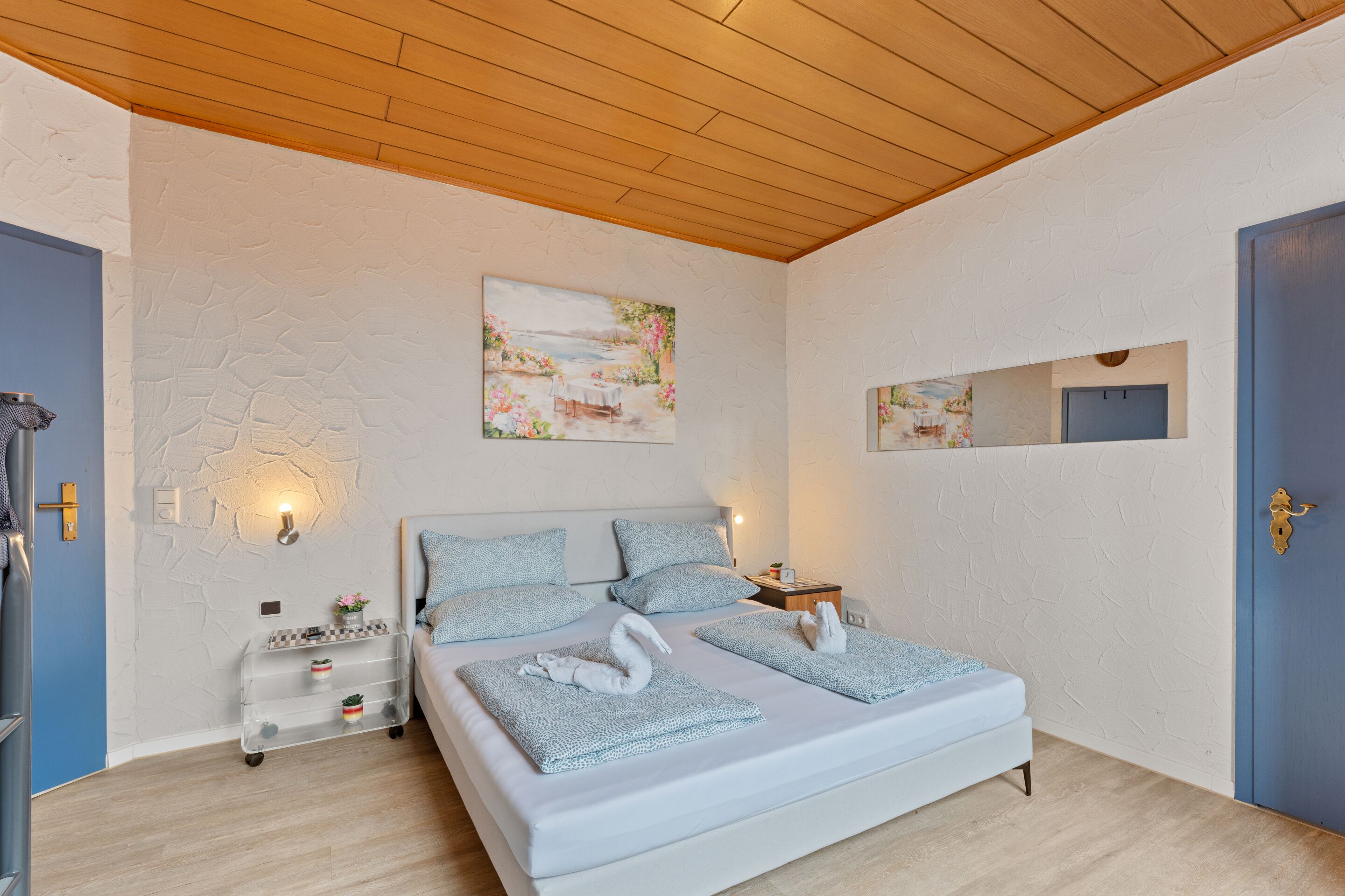 A bedroom with a large bed, two bedside tables, a wall-mounted mirror, and a painting above the bed.
