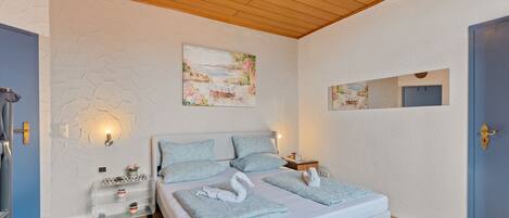A bedroom with a large bed, two bedside tables, a wall-mounted mirror, and a painting above the bed.
