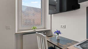 Una cocina moderna con ventana, televisor montado, radiador y una mesita con un florero.