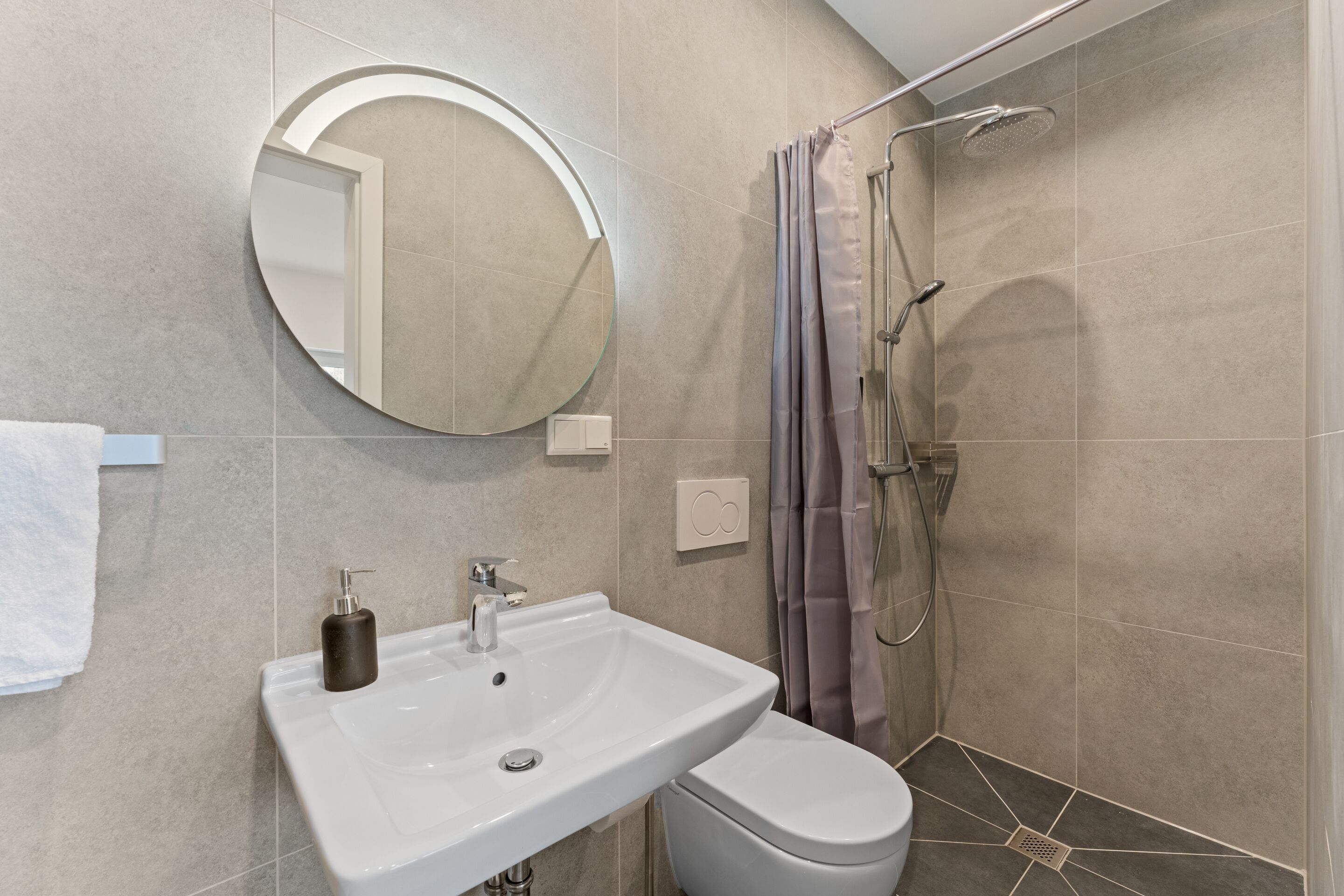A bathroom with a round mirror, a white sink, and a shower with a curtain.
