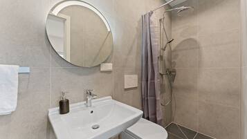 A bathroom with a round mirror, a white sink, and a shower with a curtain.