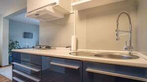 Una cocina moderna con un lavamanos de acero inoxidable, horno integrado y un televisor de pantalla plana montado en la pared.