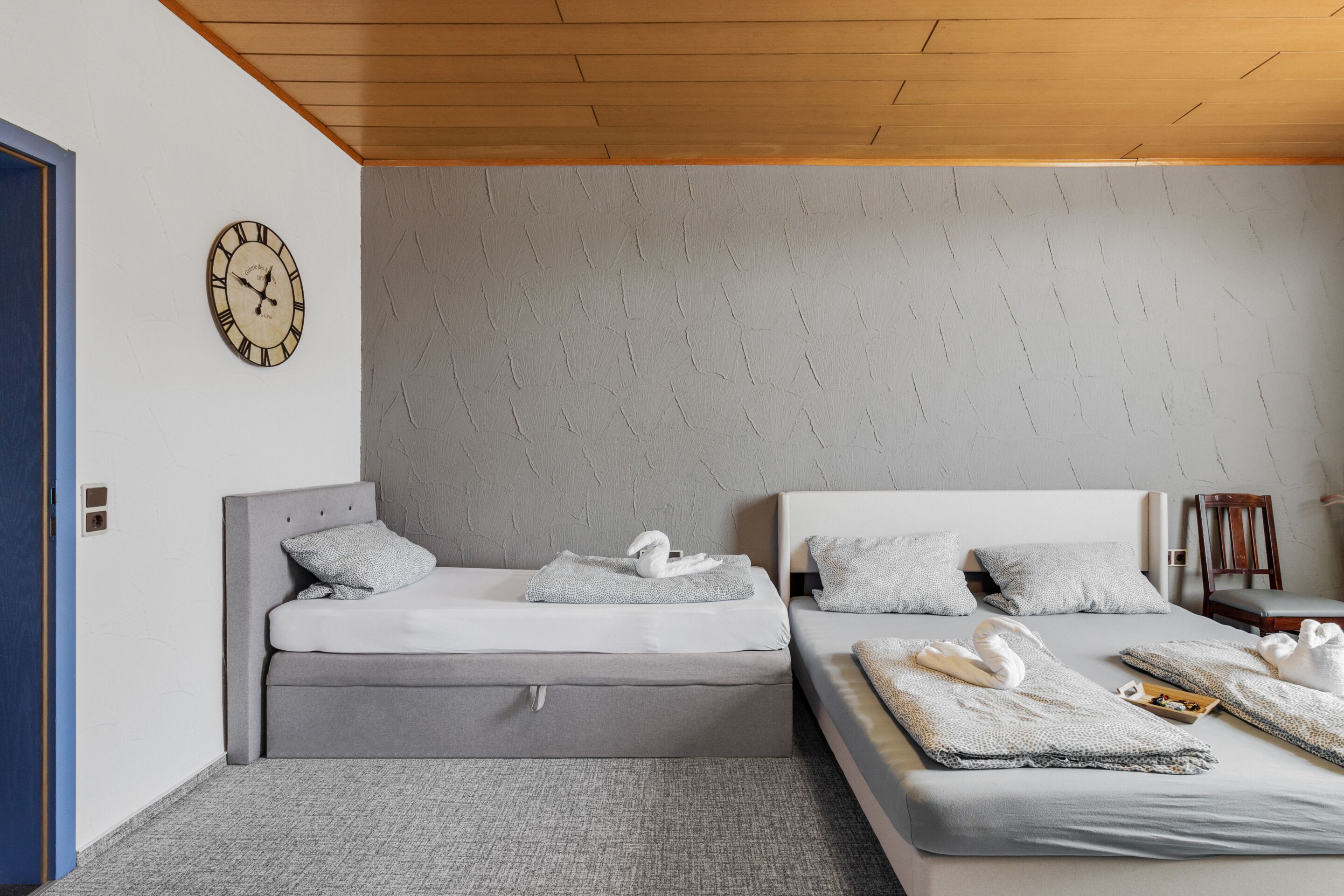 A hotel room with two beds, a clock on the wall, and towels on the beds.
