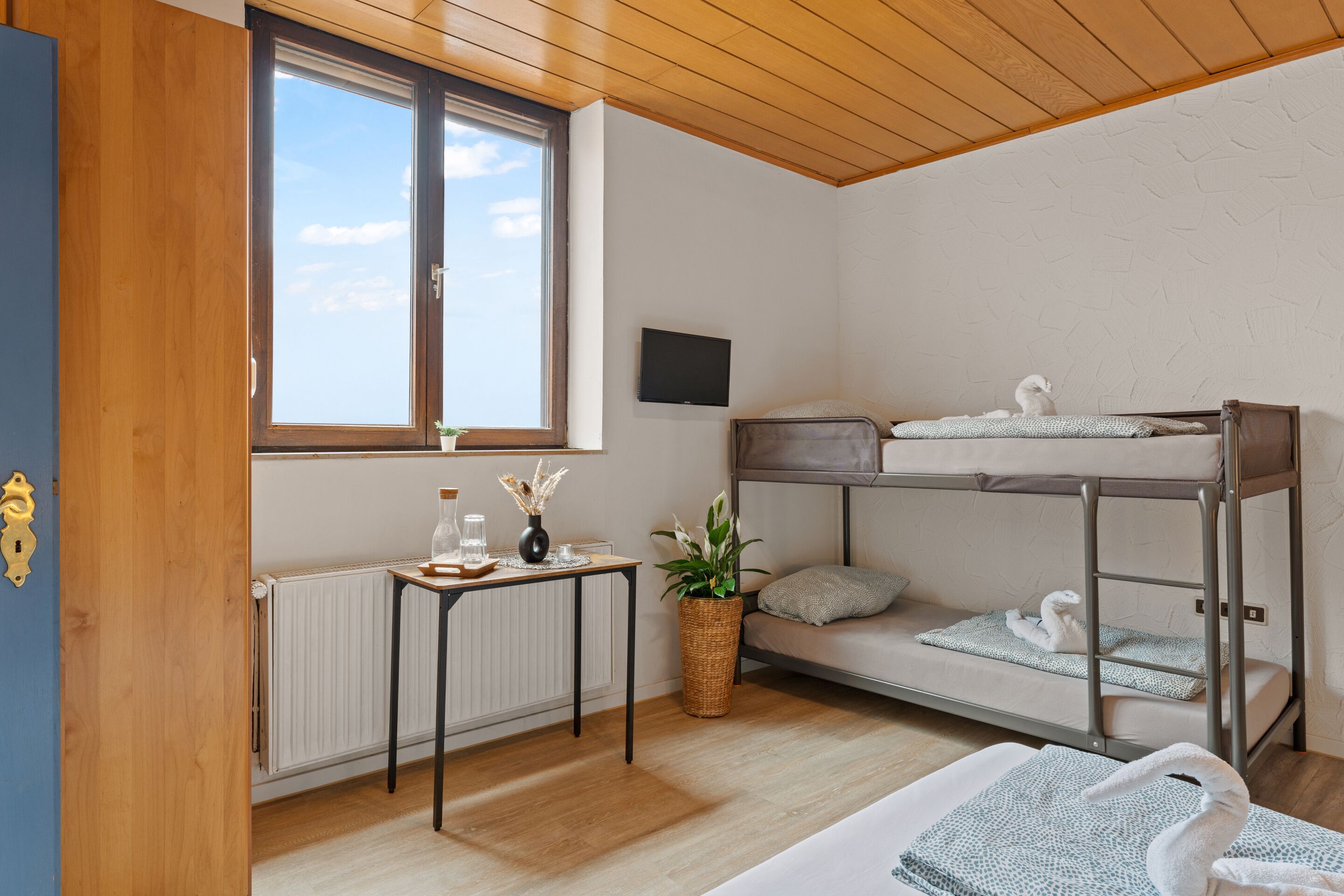 Una habitación con una cama doble, una mesita con una planta, un radiador y una ventana con vistas.