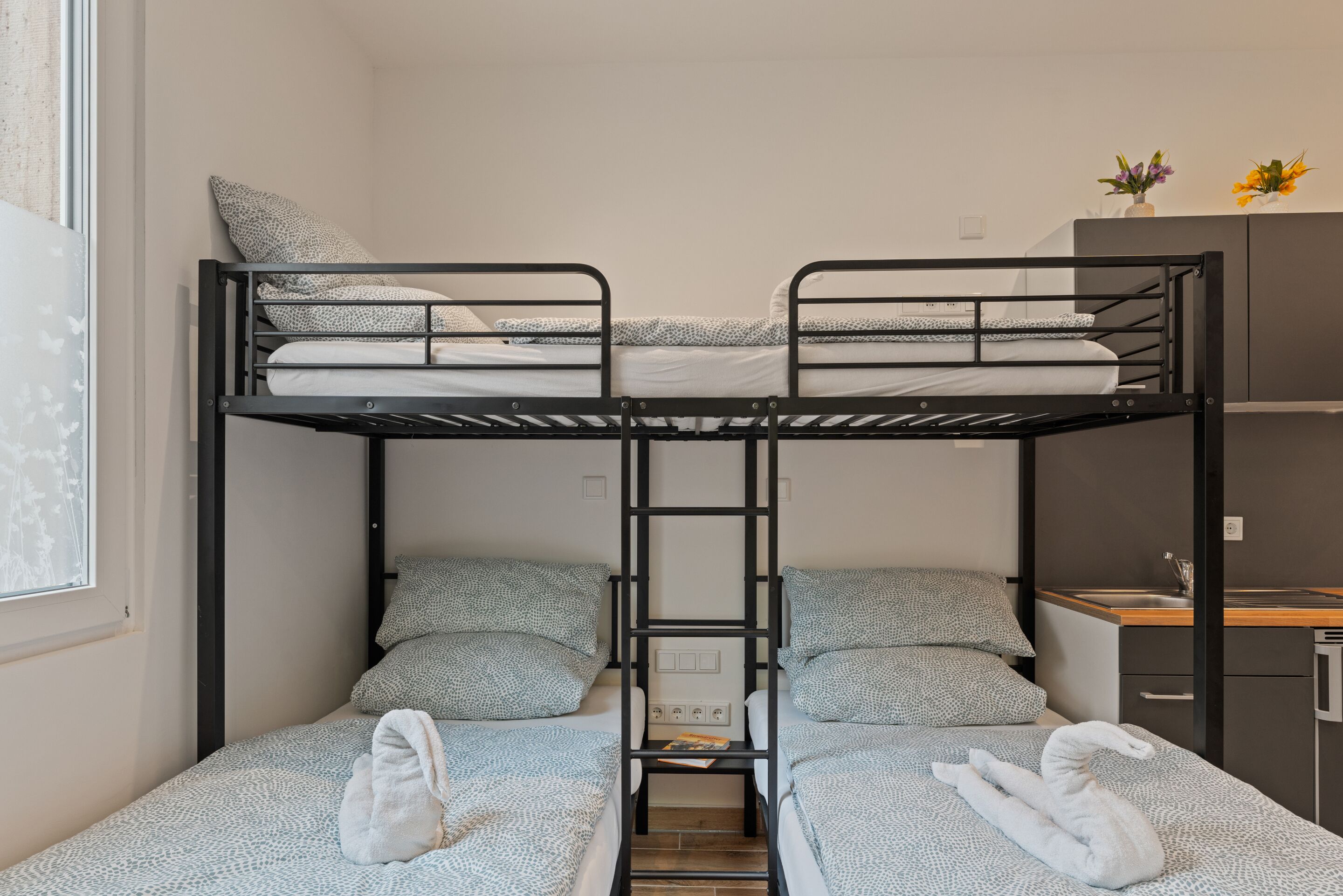 Habitació amb lliteres, escriptori i una cuineta petita.