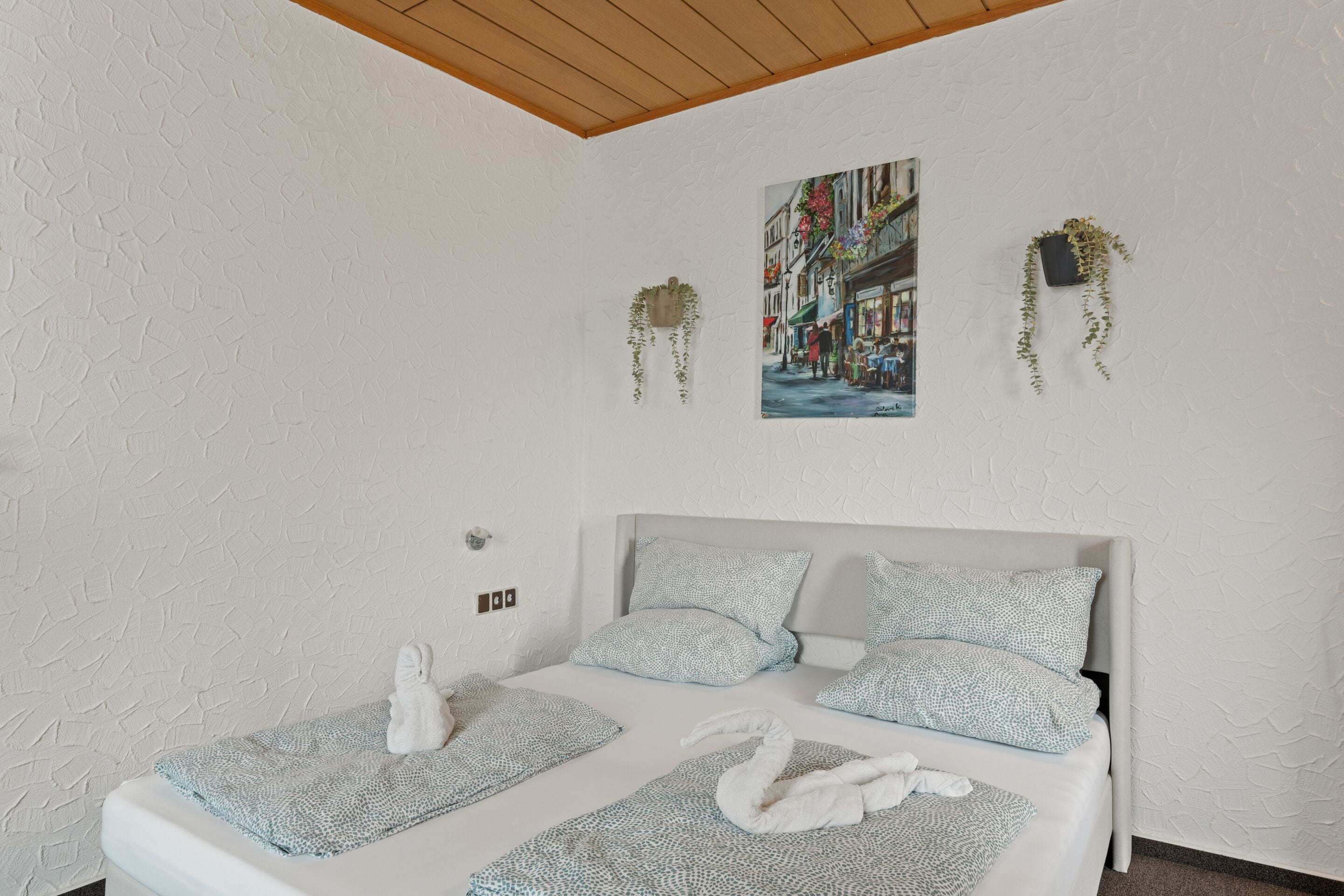 A hotel room with a bed, two pillows, a blanket, and a painting on the wall.