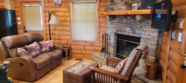 A cozy log cabin interior with a leather sofa, a wooden armchair, a fireplace, and a clock on the wall. - Cabin with mountain views all around (Sevierville)