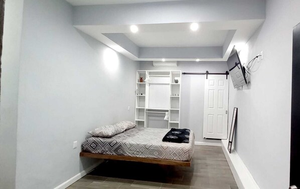 A bedroom with a bed, built-in shelving, a wardrobe, and a TV mounted on the wall.