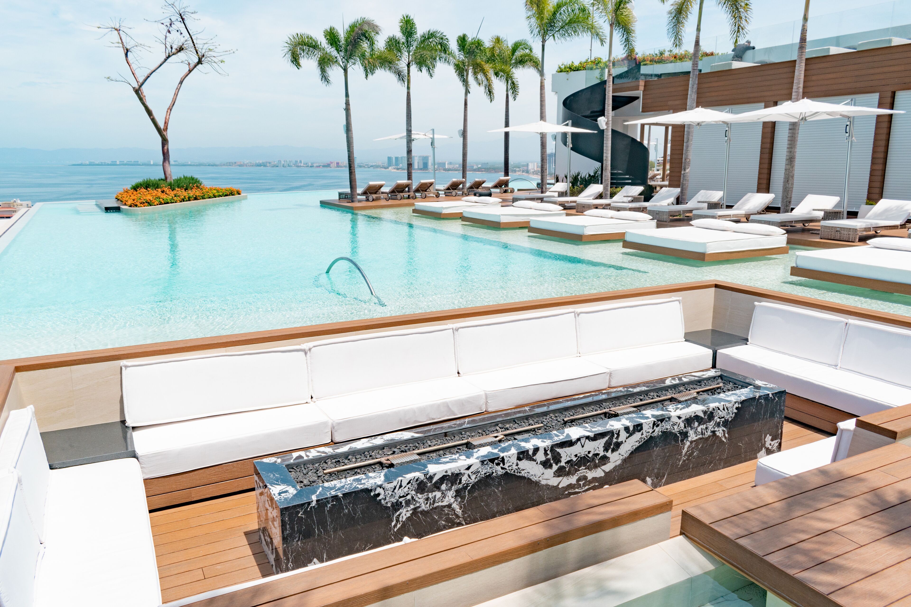 Un espace aménagé au bord de la piscine, avec des chaises longues, un foyer et une vue sur l’océan.