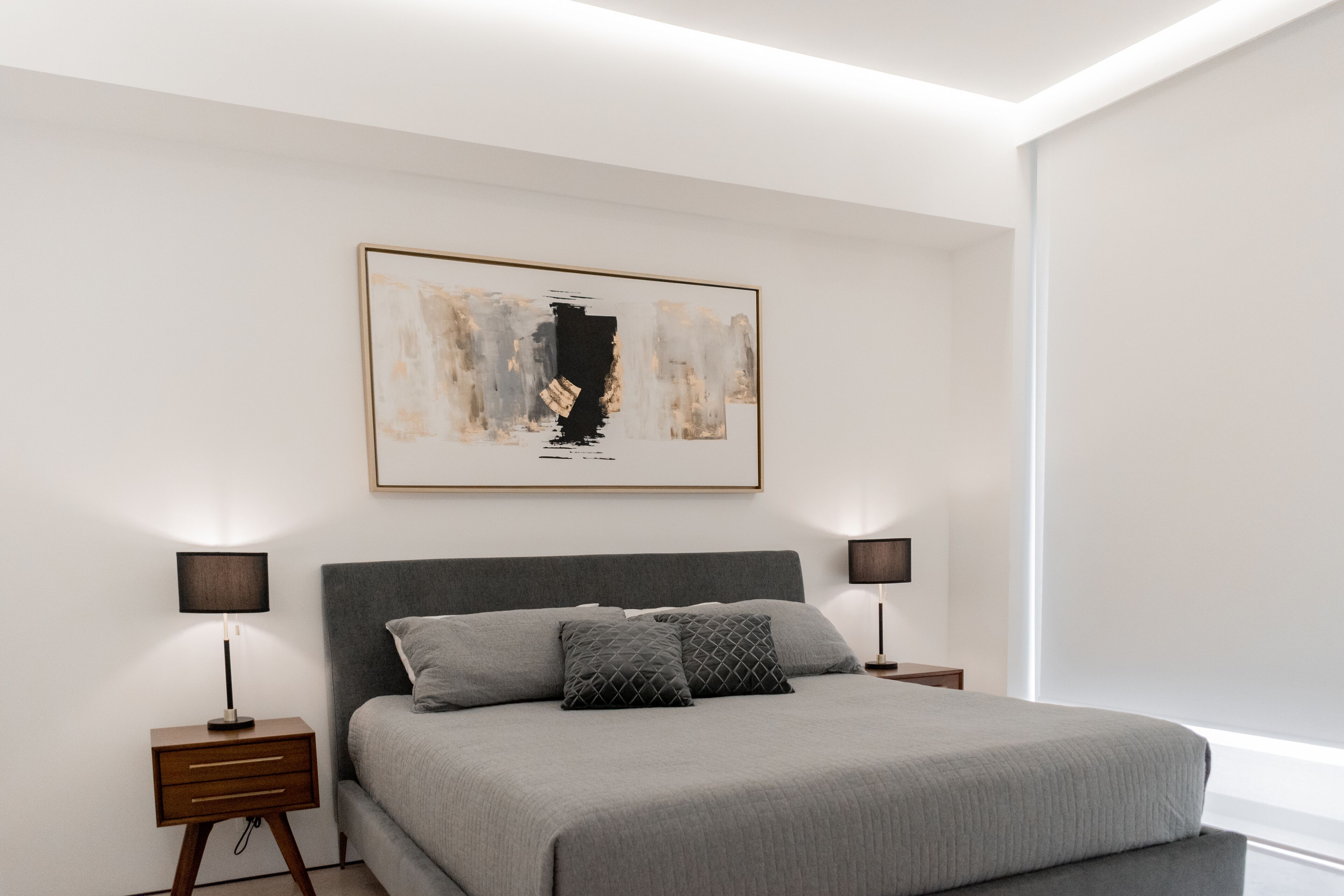 Een moderne slaapkamer met een groot bed, twee nachtkastjes en een lijst met een abstract schilderij aan de muur.