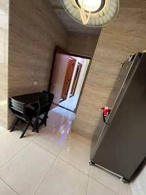 A compact kitchen with a refrigerator, a dining table with chairs, and a door leading to another room.