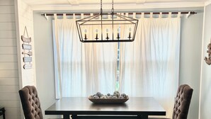 Ein Esszimmer mit einem rechteckigen Tisch, zwei Polsterstühlen, einer Bank, einer Pendelleuchte und einem Fenster mit Vorhängen.