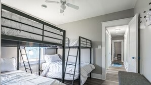 Ein Schlafraum mit Etagenbetten, Deckenventilator, einer Bank und einem Gang zu einem weiteren Raum.