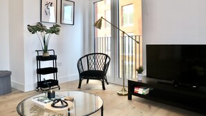 Un salon avec une table basse en verre, un fauteuil noir, un meuble TV noir et une plante posée sur une étagère noire.
