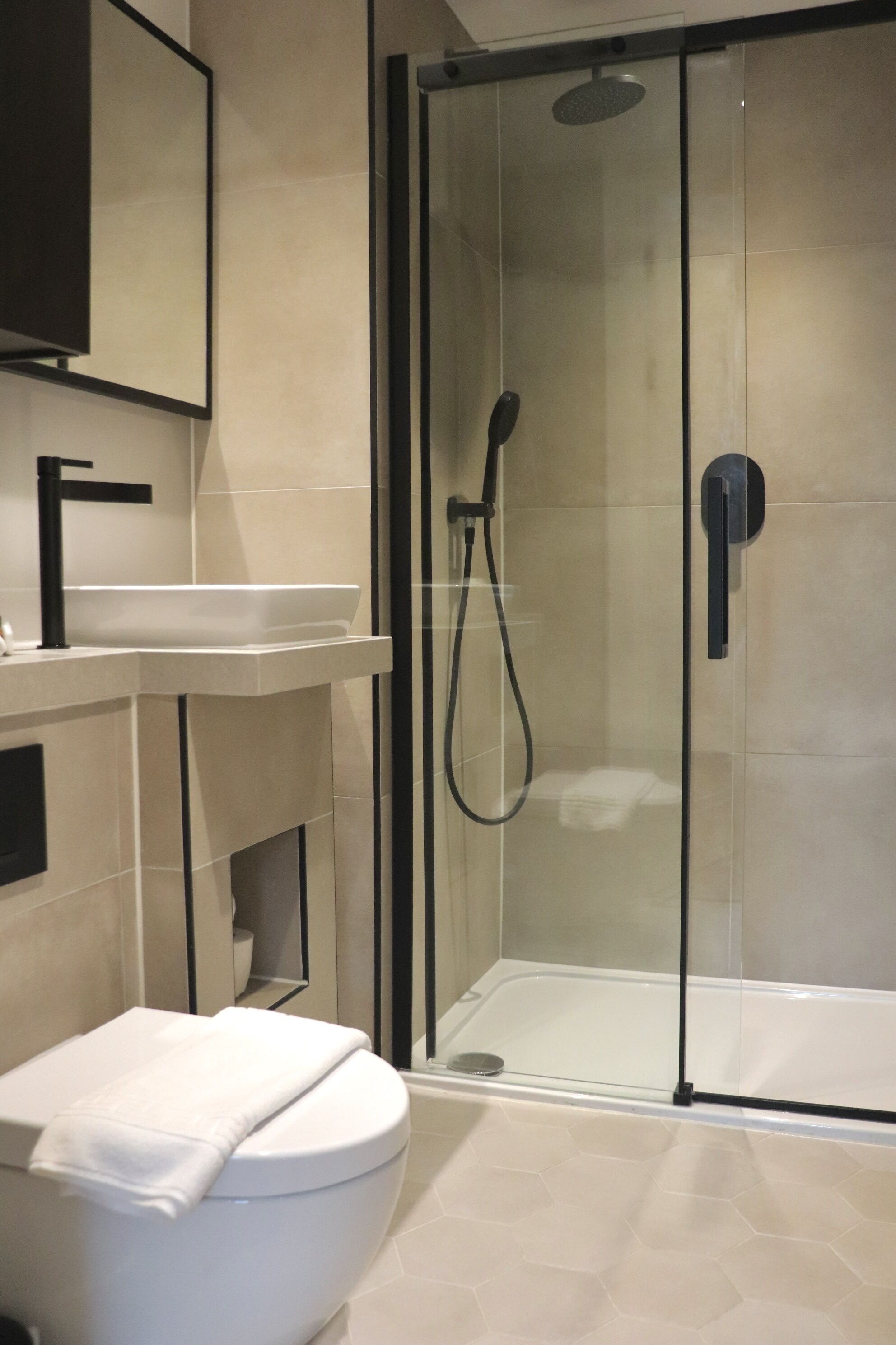 A modern bathroom with a glass-enclosed shower, a white toilet, and a sink with a black faucet.