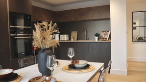 Une cuisine moderne avec des meubles en bois foncé, un four encastré et un coin repas avec une table blanche mise pour deux personnes.