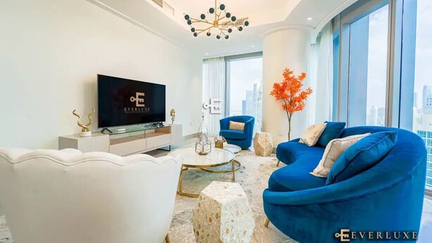 A modern living room with a large flat-screen TV, a blue sofa, a white armchair, and a coffee table.