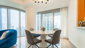 A modern living room with a blue sofa, a round dining table with four chairs, and large windows offering a city view.