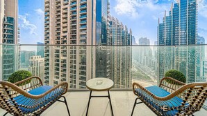 A balcony with wicker furniture and a glass table, overlooking a cityscape with high-rise buildings.