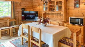 Een houten blokhut interieur met een eettafel, stoelen, een televisie, een kast met glazen deuren en een magnetron.
