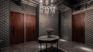 Une pièce avec une table ronde, deux portes en bois, un lustre et un mur orné de motifs.