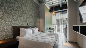 Une chambre moderne avec un grand lit, une petite table avec des chaises et une vue sur la ville grâce à de grandes fenêtres.