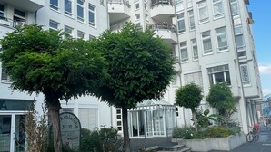 Un bâtiment moderne à étages, doté de balcons et d’un jardin bien entretenu, agrémenté d’arbres et d’arbustes.