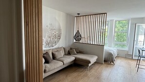 Un salon moderne avec un canapé d’angle, une cloison en bois et une grande fenêtre qui laisse entrer la lumière naturelle.
