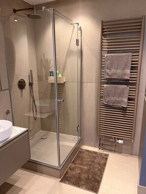 Enjoy a refreshing shower in the bathroom, featuring a glass-enclosed shower with a handheld showerhead and wall-mounted faucet.