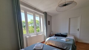 Ein Hotelzimmer mit zwei Betten, einem Heizkörper, einem Fenster mit Vorhängen, einer Tür und einer Pendelleuchte.