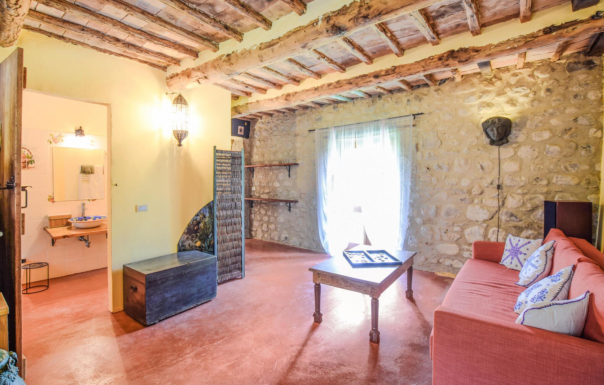 Un interno rustico con travi a vista in legno, una parete in pietra, una panca di legno, un divano e un tavolino con un gioco da tavolo.