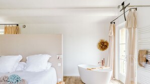 Un dormitorio moderno con una cama grande, una bañera independiente y un ventanal con cortinas.