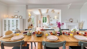 Un comedor con una mesa de madera preparada para el desayuno, con platos, tazones y frutas.