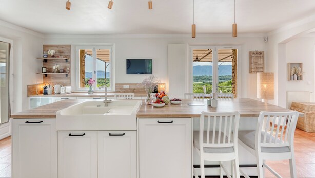 Una cocina moderna con una isla grande, muebles blancos y vistas al exterior.