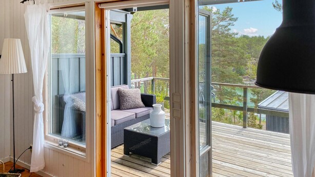 A balcony with a sofa and cushions, a small table with a vase, and a view of trees and a lake.