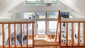 A spacious attic room with a sloped ceiling, wooden railings, and large windows offering views of the outside.