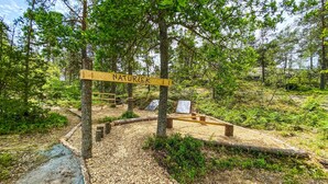 A wooden sign with the word "NATUREK" in a forested area with a dirt path.