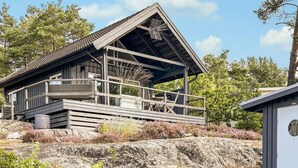 A wooden cabin with a balcony, surrounded by natural vegetation and rocks.